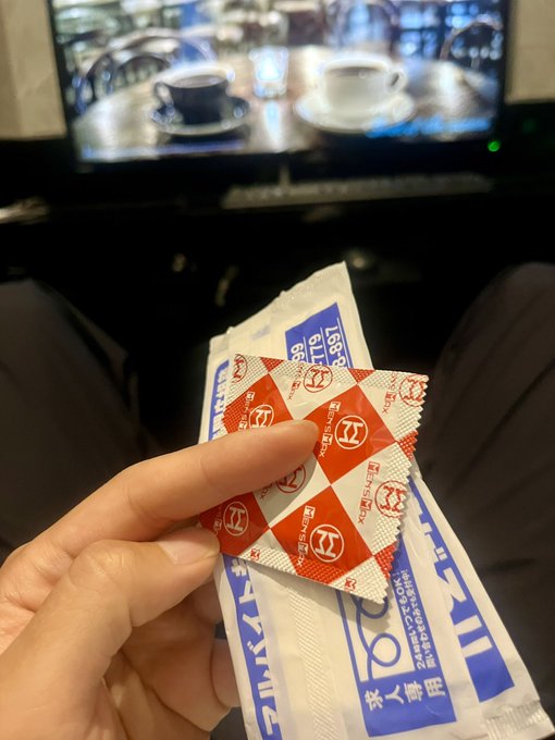 A hand holding small red-and-white checkered Japanese condiment packets (likely spice mix) in front of a TV displaying coffee cups.