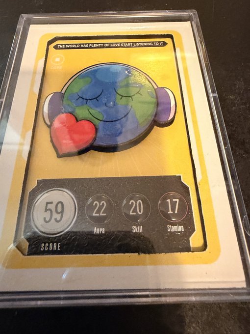 A handmade trading card featuring a watercolor Earth character with closed eyes hugging a red heart, titled 'THE WORLD HAS PLENTY OF LOVE START LISTENING TO IT', with stats showing a Score of 59, 22 Aura, 20 Skill, and 17 Stamina.