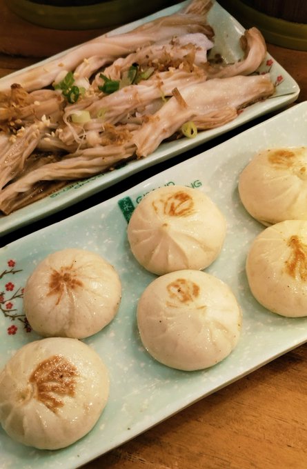 Two plates of Chinese food: a long dish with shredded meat and scallions, and a rectangular plate holding six pan-fried soup dumplings (xiaolongbao) with golden tops.