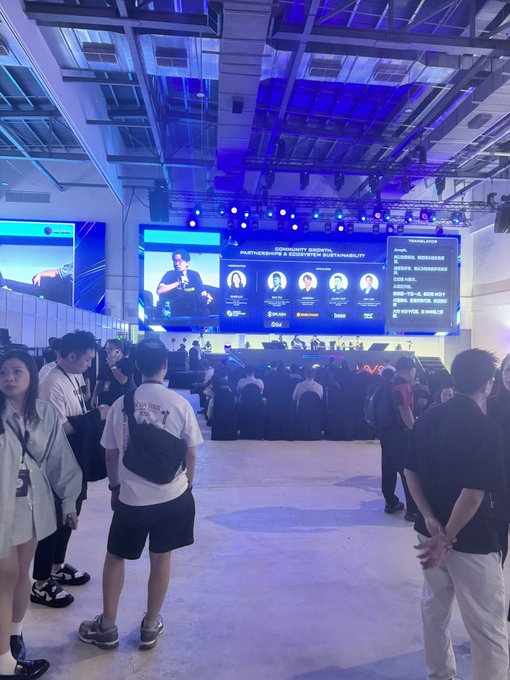 A crowd of people stands at an indoor tech or crypto conference watching a panel discussion titled 'COMMUNITY GROWTH, PARTNERSHIPS & CONTENT SUSTAINABILITY' with speakers displayed on a large screen.