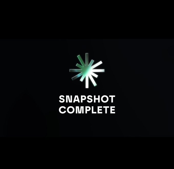A dark loading screen displays a glowing green starburst icon above the white text "SNAPSHOT COMPLETE."
