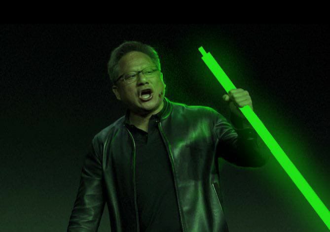 A man wearing glasses and a black leather jacket passionately holds up a glowing green lightsaber-like stick against a dark background.