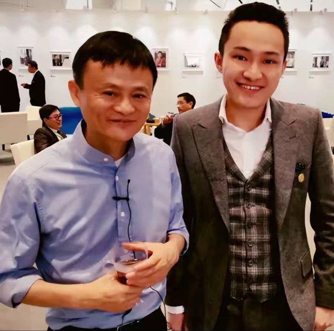 A photo showing Justin Sun (left) standing alongside Tron CEO Justin Sun at what appears to be a tech conference or event, with Sun wearing a blue button-down shirt while holding a drink. The caption references Sun's earlier promise to fund dental work for "Brother Sun" upon his return to China, with the image capturing their in-person reunion at this professional gathering.