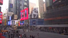 A street-level view of Times Square in New York City, showing crowded sidewalks, yellow taxis, and illuminated billboards.