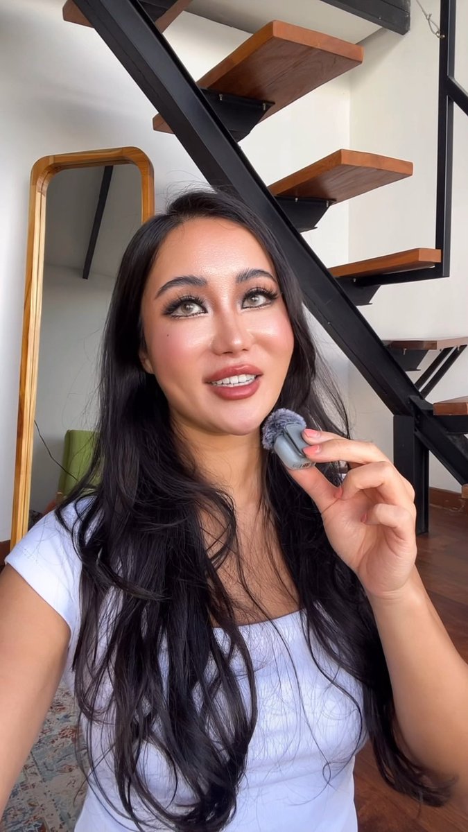 A woman in a white off-shoulder top applies makeup while holding a mic in front of a modern staircase, smiling upward as she engages with content creation.

The image likely represents the "crypto girls" referenced in the post—showcasing a woman who is already actively participating in the crypto space and educating newcomers, aligning with the call for genuine, knowledgeable female voices spearheading the movement rather than just anyone joining for clout.