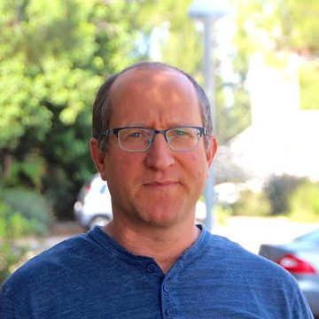 A headshot of a middle-aged man wearing glasses and a blue henley shirt, photographed outdoors.