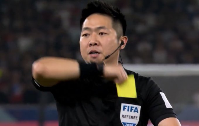 iced tea is served to the referee during a soccer match, with a blurred stadium background and a yellow "FIFA REFEREE" badge on his shirt.