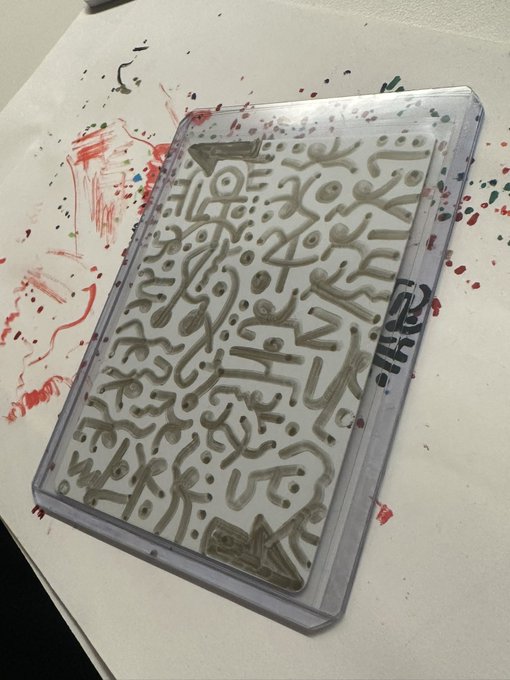An acrylic tray with raised Arabic calligraphy design sitting on a table covered in multicolored paint splatters and smears.