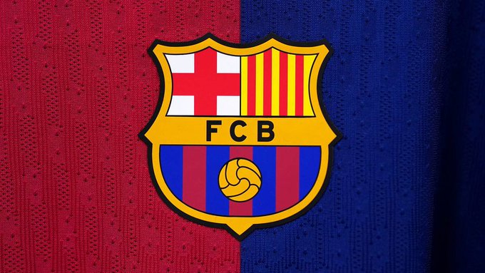 Close-up of the FC Barcelona (FCB) club crest featuring the red cross, Catalan stripes, and Senyera on the traditional claret and blue kit fabric.