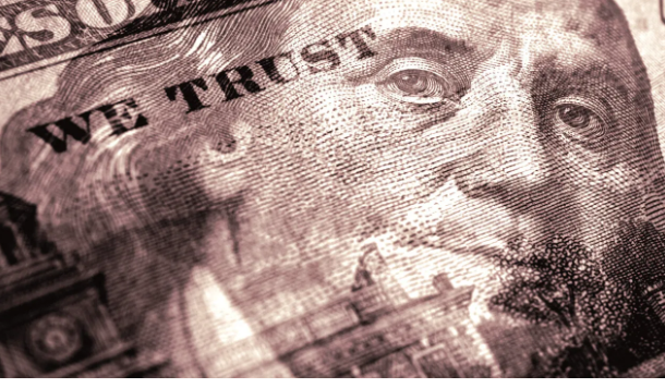 A close-up sepia-toned photograph of a US hundred-dollar bill focusing on Benjamin Franklin's face and the 'IN WE TRUST' text.