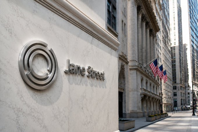 The exterior of a building displaying the 'Jane Street' logo and signage on a white marble wall, with American flags and a city street visible to the right.