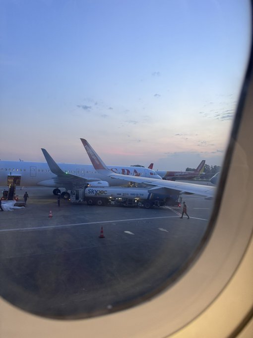View from an airplane window at dusk, showing parked aircraft and a "SkyPAC" fuel truck on the tarmac, as the traveler arrives in Vietnam for the upcoming Conviction blockchain conference.