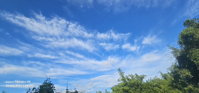 The image shows a beautiful blue sky with white clouds, which appears to be taken from below. The sky has a hazy appearance due to the presence of clouds. The photo is posted by someone named "XOOB Network" on social media, possibly sharing their experience or appreciation for the view.