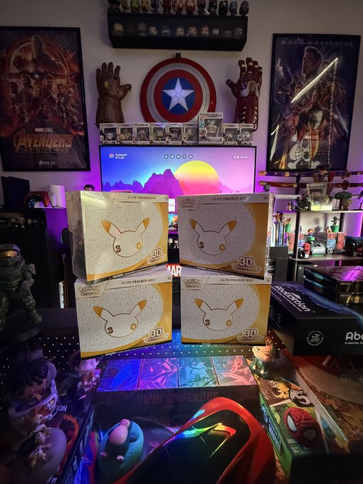 A collection room filled with pop culture memorabilia including Marvel posters, an Infinity Gauntlet, and four Eevee Elite Trainer Boxes stacked on a desk.