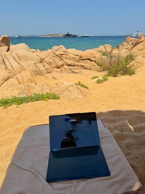 A dual-screen laptop rests on a beach towel overlooking a rocky Mediterranean coastline with yachts anchored offshore, embodying the "back to relaxing" promise after a bold $15K memecoin aping play set for sale at a $5 million market cap.