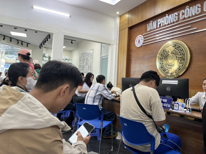 People seated at counters inside what appears to be a Vietnamese government office ('VĂN PHÒNG CÔNG') with a large emblem on the wall.
