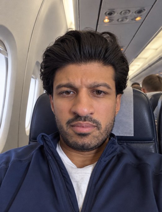A man takes a selfie while seated on an airplane, with the cabin interior visible behind him. The image captures his in-flight travel experience, complementing his post about BTC hitting 86k and his "OSF flight indicator" signaling a successful journey with a Korean greeting ("annyeonghaseyo").