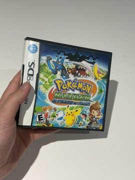 A hand holding a Nintendo DS game case for Pokémon Trozei! in its original Japanese release, featuring Pikachu and other Pokémon on the cover art.