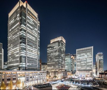 A nighttime skyline of Tokyo's modern financial district, with illuminated skyscrapers towering over a lit plaza, illustrates the presence of major financial institutions like SBI in Japan's economic landscape. The image visually anchors the post's message that traditional financial giants are increasingly engaging with blockchain technology through partnerships with organizations like the Solana Foundation.