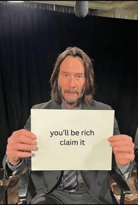 Actor Keanu Reeves sits in a chair against a black curtain backdrop, holding a white sign that reads 'you'll be rich claim it.'