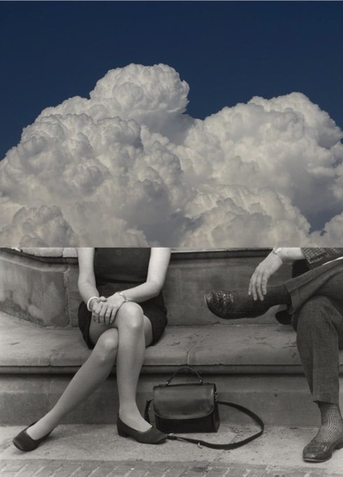 A black-and-white photograph showing two people sitting on a ledge beneath a massive cumulus cloud that appears to erupt from the wall behind them.