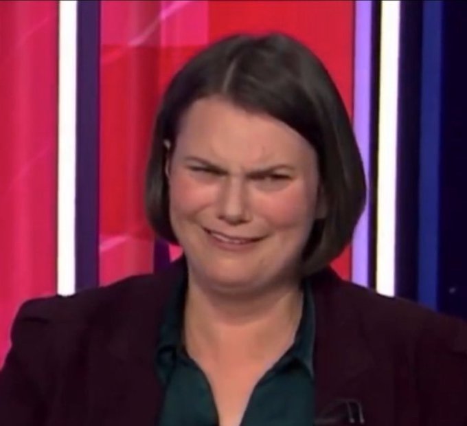 The image features a woman wearing a brown blazer, sitting at a table with her head tilted back as if she's making a funny face for the camera. The background of the image consists of red and blue stripes, which are likely part of an advertisement or promotional material. There is also text in the image that reads "Your average $STRC shill when they find out @Strategy is not legally obligated to actually pay the dividend or keep the peg." This suggests that there might be a connection between the woman's facial expression and the content displayed on the background, possibly indicating an advertisement for a company related to the stock market.