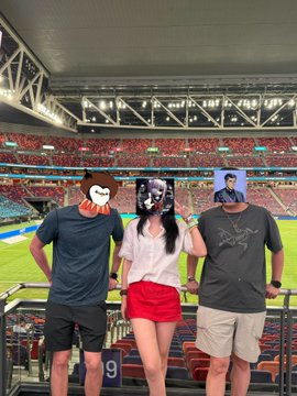 Three people stand in a stadium with their faces covered by cartoon and image overlays, with the stands visible behind them filled with spectators.