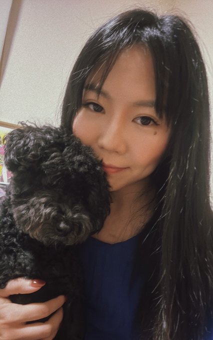 A selfie of a woman with long dark hair holding a small curly black dog close to her face.