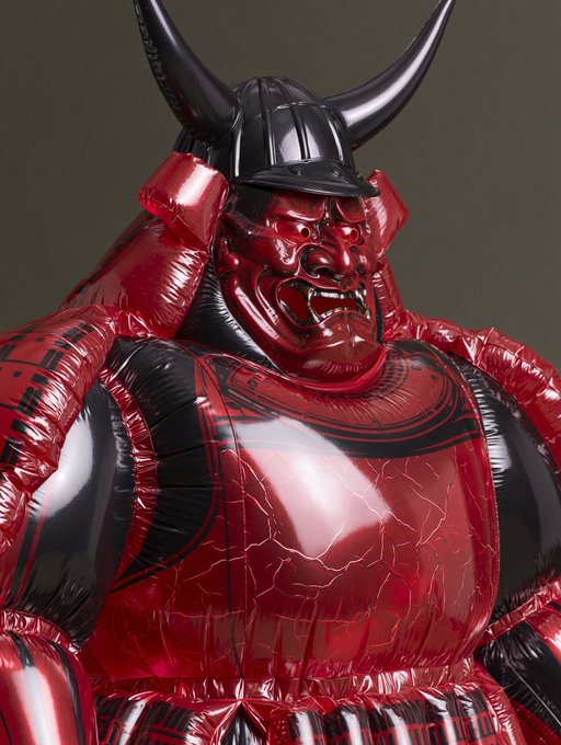 A red and black inflatable samurai warrior figure with a fierce Hannya mask and horned helmet, featuring Japanese text on the shoulder.