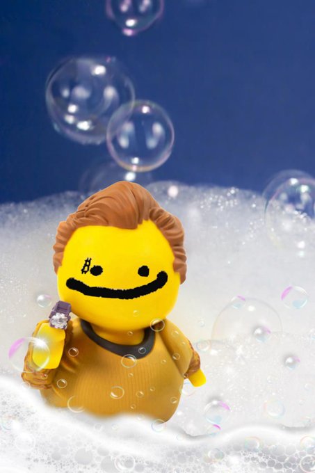 A small LEGO minifigure with a yellow smiley face and brown hair, taking a bubble bath surrounded by floating soap bubbles.