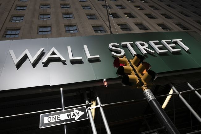 A street sign reading "WALL STREET" stands prominently against a tall building, accompanied by a "ONE WAY" sign and a traffic light below. The iconic Wall Street imagery visually reinforces the post's message about BNB Chain emerging as a major gateway for tokenized stocks and ETFs in traditional finance.