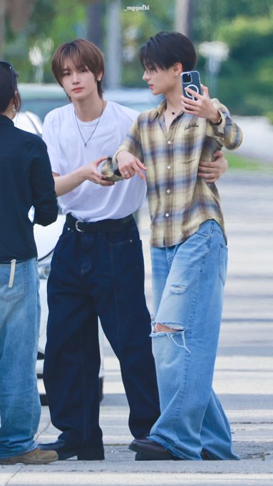 Two young men taking a mirror selfie outdoors; one wears a plaid shirt and ripped jeans while the other wears a white t-shirt and dark pants, credited to '_seagullbl'.