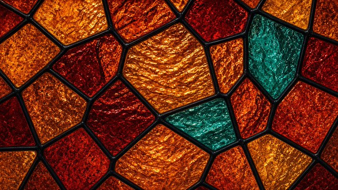 A close-up of a stained glass window featuring textured orange, red, and teal geometric panels outlined in black lead.