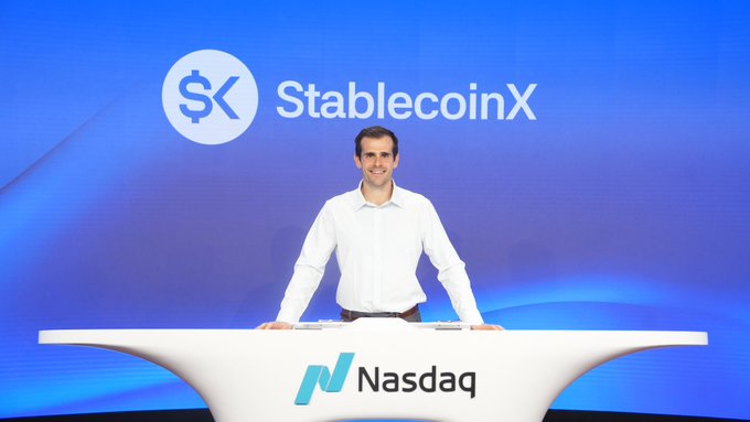 A man in a white shirt smiling behind a Nasdaq podium with 'StablecoinX' displayed on the screen behind him.