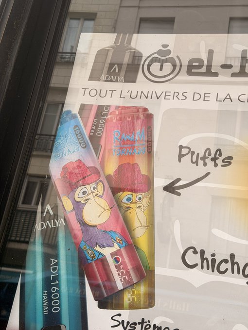 A storefront window advertises vape/e-cigarette products featuring "ADALYA DL 16000" devices with cartoon monkey branding alongside French text like "TOUT L'UNIVERS DE LA CIG" and "Puffs"—though nothing in the image actually relates to NFTs, making the caption's connection purely incidental.