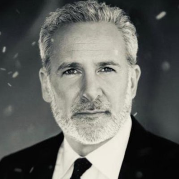 A black and white portrait of a gray-haired, bearded man in a dark suit and tie looking directly at the camera against a dark, speckled background.