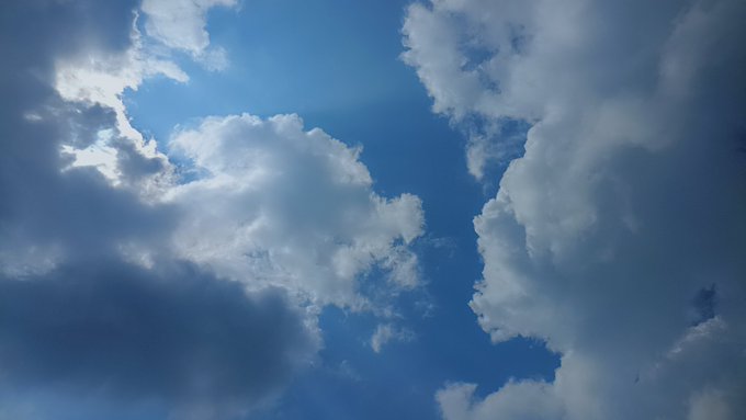 A dramatic sky filled with billowing white and gray clouds is illuminated by sunlight breaking through, with patches of blue sky visible.