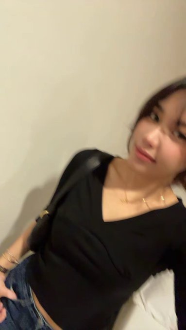A young woman with dark hair, wearing a black V-neck top and delicate necklace, takes a slightly blurred selfie with a soft, candid expression—her relaxed demeanor contrasting with the post's confession of failed memecoin and LP investments, hinting at a reflective moment after financial setbacks.