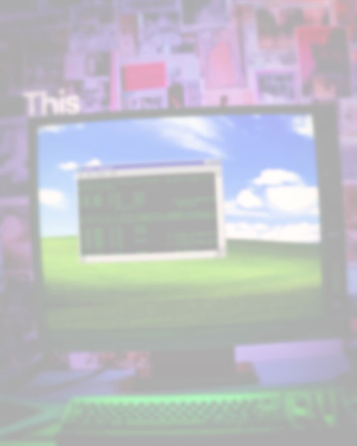 The image shows an old computer monitor displaying a green screen that says "This" at the top of the monitor, with a picture of a field below it. The monitor has a keyboard and mouse attached to its right side. In the background, there is a wall covered in various posters and pictures.