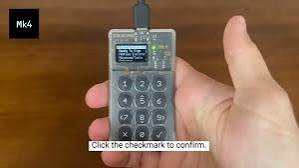 A small gray electronic device labeled 'M4' is held in a hand, with on-screen text instructing to 'Click the checkmark to confirm.'