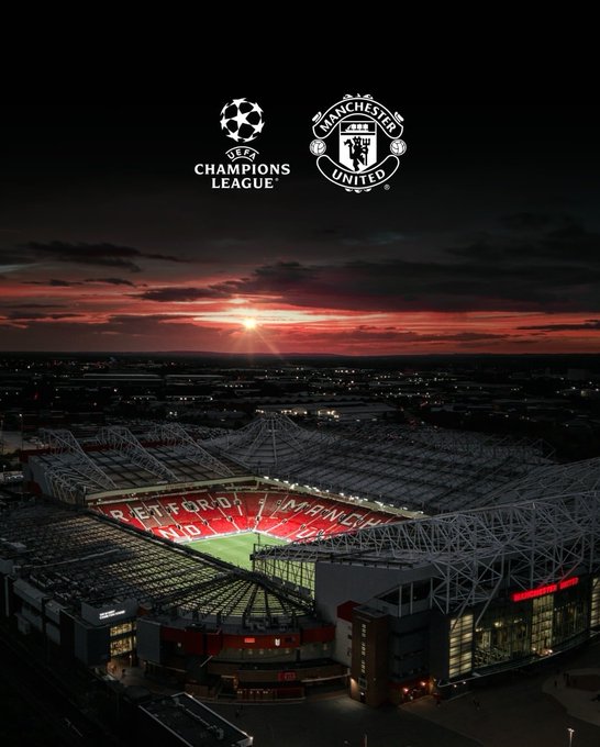 The image features a large stadium at night, lit up by lights that create an impressive atmosphere. The stadium appears to be a soccer field or a similar venue, with its lights illuminating the area. In the background, there are logos for Manchester United and the Champions League, indicating that this is likely a sports event taking place in Manchester.