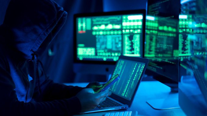 A hooded figure works on a laptop beside glowing monitors displaying streams of code, evoking the stealthy cyber operation behind the reported $BTC cold-wallet breach that has now compromised 4,500 addresses and nearly $89 million in losses.
