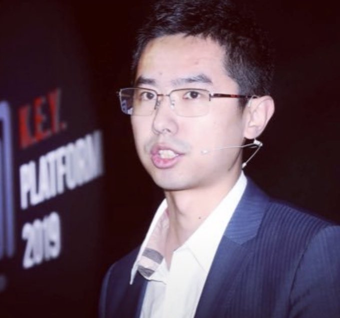 An Asian man with glasses and a headset microphone speaks at an event, with a backdrop displaying 'LPL PLAYOFFS 2019'.