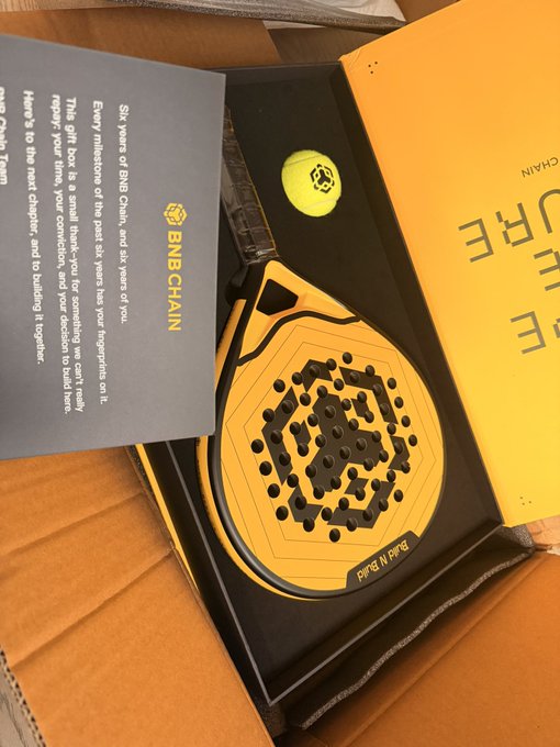 A BNB Chain branded merchandise package inside a yellow box, containing a yellow headphone-shaped item and a thank-you card.