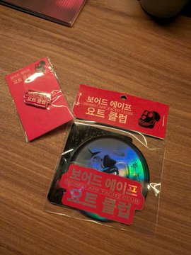 Korean merchandise packaging labeled '본이드에이프 오토 콜러' (Bonded Ape Auto Caller) containing a circular accessory, displayed on a wooden surface.