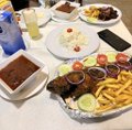 An overhead view of a meal on a tray featuring a hamburger steak with vegetables, french fries, a soft-serve ice cream cone, and other side dishes.
