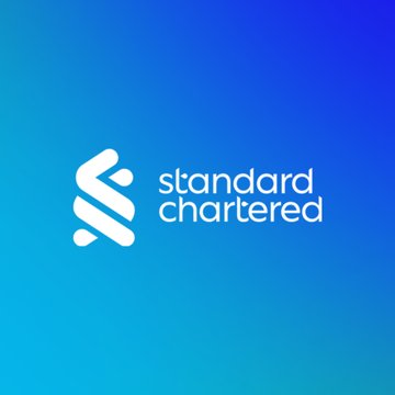 The image shows the Standard Chartered logo, a white emblem with the company name "standard chartered" displayed on a blue gradient background, representing the bank issuing the bullish Bitcoin price prediction mentioned in the post.