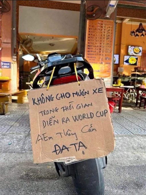 The image features a motorcycle that has been repurposed as a makeshift outdoor seating area for a restaurant, with a sign hung up on its back. The sign appears to be written in another language but still conveys information about the establishment. There are also other signs present in the scene, providing additional details about the restaurant or nearby businesses.