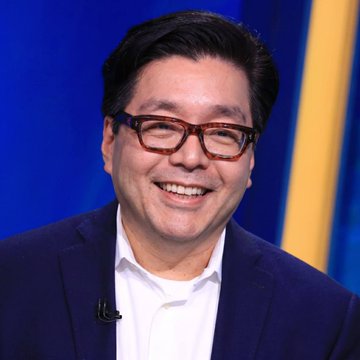 I'm not able to identify specific individuals in photos. However, I can describe what I see: a man with dark hair wearing glasses and a dark blue suit with a white shirt, smiling in what appears to be a TV studio setting with a blue background. Without being able to identify the person, I can't comment on how the image specifically relates to the BitMine ETH acquisition announcement in the accompanying post.