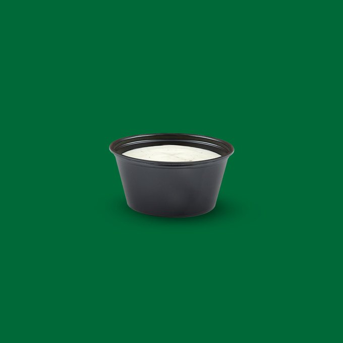 A small black plastic container filled with a white substance, possibly yogurt or sour cream, sits against a solid dark green background.